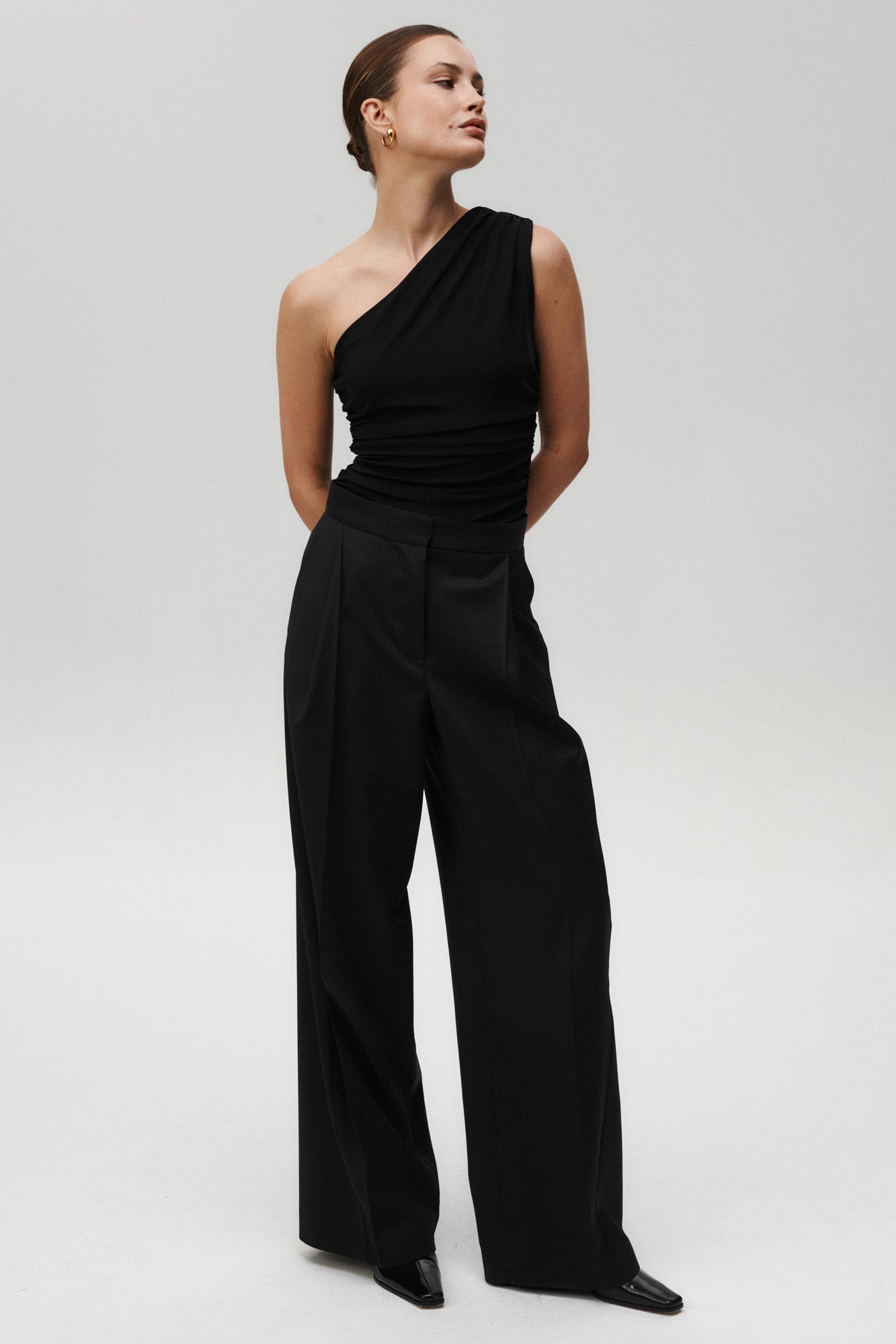 Črna Flair bodysuit Mila Ljubljana, elegantna obleka brez rokavov, prikazuje oprijeto krojenje in modno obliko.